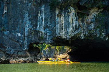 Ha Long, VİETNAM MAR 12 2023: Ha Long Körfezi 'ndeki kireçtaşı kayaların arasında yüzen turist hurdaları, Halong Körfezi, Vietnam yakınlarındaki Lan Ha Körfezi' ndeki bir mağarada kano yapan insanlar.