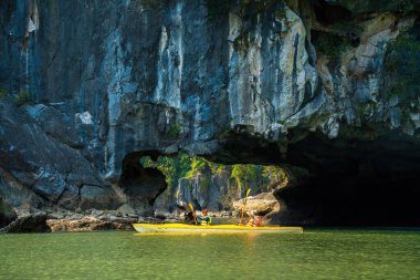 Ha Long, VİETNAM MAR 12 2023: Ha Long Körfezi 'ndeki kireçtaşı kayaların arasında yüzen turist hurdaları, Halong Körfezi, Vietnam yakınlarındaki Lan Ha Körfezi' ndeki bir mağarada kano yapan insanlar.