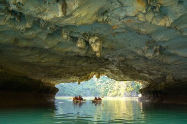 Ha Long, VİETNAM MAR 12 2023: Ha Long Körfezi 'ndeki kireçtaşı kayaların arasında yüzen turist hurdaları, Halong Körfezi, Vietnam yakınlarındaki Lan Ha Körfezi' ndeki bir mağarada kano yapan insanlar.