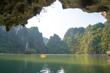 Ha Long Körfezi 'ndeki kireçtaşı kayalarının arasında yüzen turist hurdaları, Halong Körfezi, Vietnam yakınlarındaki Lan Ha Körfezi' ndeki bir mağarada kano yapan insanlar.