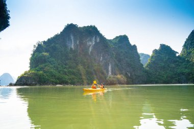 Ha Long, VİETNAM MAR 12 2023: Ha Long Körfezi 'ndeki kireçtaşı kayaların arasında yüzen turist hurdaları, Halong Körfezi, Vietnam yakınlarındaki Lan Ha Körfezi' ndeki bir mağarada kano yapan insanlar.