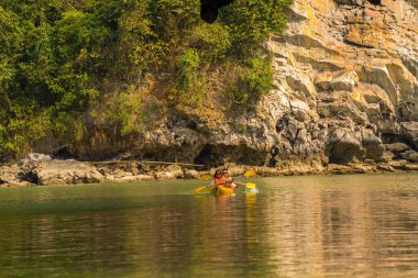Ha Long Körfezi 'ndeki kireçtaşı kayalarının arasında yüzen turist hurdaları, Halong Körfezi, Vietnam yakınlarındaki Lan Ha Körfezi' ndeki bir mağarada kano yapan insanlar.