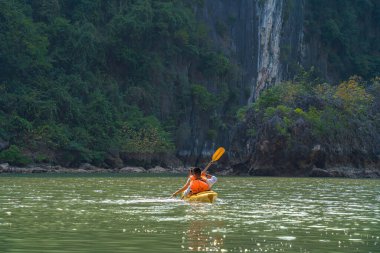 Ha Long Körfezi 'ndeki kireçtaşı kayalarının arasında yüzen turist hurdaları, Halong Körfezi, Vietnam yakınlarındaki Lan Ha Körfezi' ndeki bir mağarada kano yapan insanlar.