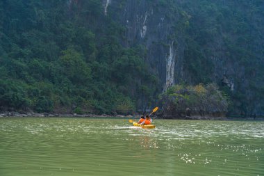 Ha Long Körfezi 'ndeki kireçtaşı kayalarının arasında yüzen turist hurdaları, Halong Körfezi, Vietnam yakınlarındaki Lan Ha Körfezi' ndeki bir mağarada kano yapan insanlar.
