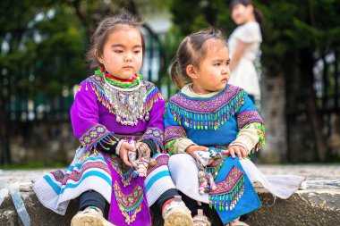 Lao Cai, VIETNAM - MAR 12 2023: Vietnamlı küçük bir kızın güzel portresi HMong etnik azınlığı kilisenin önünde oturan turistleri selamlıyor ve el yapımı eşyalar satıyor. Sapa şehir merkezinde.