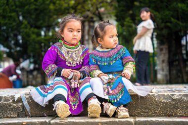 Lao Cai, VIETNAM - MAR 12 2023: Vietnamlı küçük bir kızın güzel portresi HMong etnik azınlığı kilisenin önünde oturan turistleri selamlıyor ve el yapımı eşyalar satıyor. Sapa şehir merkezinde.