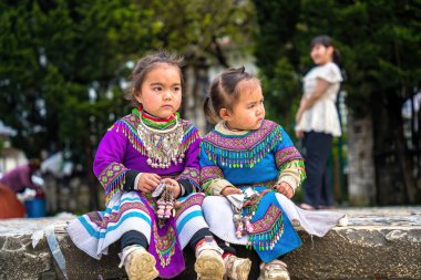 Lao Cai, VIETNAM - MAR 12 2023: Vietnamlı küçük bir kızın güzel portresi HMong etnik azınlığı kilisenin önünde oturan turistleri selamlıyor ve el yapımı eşyalar satıyor. Sapa şehir merkezinde.