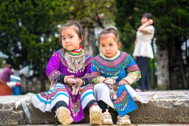 Lao Cai, VIETNAM - MAR 12 2023: Vietnamlı küçük bir kızın güzel portresi HMong etnik azınlığı kilisenin önünde oturan turistleri selamlıyor ve el yapımı eşyalar satıyor. Sapa şehir merkezinde.