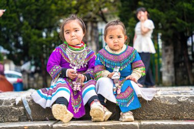 Lao Cai, VIETNAM - MAR 12 2023: Vietnamlı küçük bir kızın güzel portresi HMong etnik azınlığı kilisenin önünde oturan turistleri selamlıyor ve el yapımı eşyalar satıyor. Sapa şehir merkezinde.