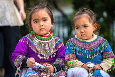 Lao Cai, VIETNAM - MAR 12 2023: Vietnamlı küçük bir kızın güzel portresi HMong etnik azınlığı kilisenin önünde oturan turistleri selamlıyor ve el yapımı eşyalar satıyor. Sapa şehir merkezinde.