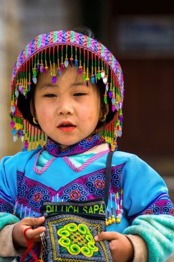 Lao Cai, VIETNAM - MAR 12 2023: Vietnamlı küçük bir kızın güzel portresi HMong etnik azınlığı kilisenin önünde oturan turistleri selamlıyor ve el yapımı eşyalar satıyor. Sapa şehir merkezinde.