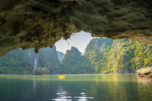 Ha Long Körfezi 'ndeki kireçtaşı kayalarının arasında yüzen turist hurdaları, Halong Körfezi, Vietnam yakınlarındaki Lan Ha Körfezi' ndeki bir mağarada kano yapan insanlar.