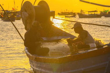 Vung Tau, VIETNAM MAR 25 2023: Balıkçı ağlarını gün doğumunda ya da günbatımında tekneye atıyor. Geleneksel balıkçılar balık ağını hazırlıyor.