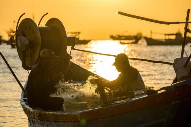 Vung Tau, VIETNAM MAR 25 2023: Balıkçı ağlarını gün doğumunda ya da günbatımında tekneye atıyor. Geleneksel balıkçılar balık ağını hazırlıyor.