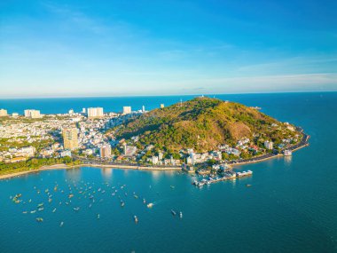 Vung Tau city aerial view with beautiful sunset and so many boats. Panoramic coastal Vung Tau view from above, with waves, coastline, streets, coconut trees and Tao Phung mountain in Vietnam.
