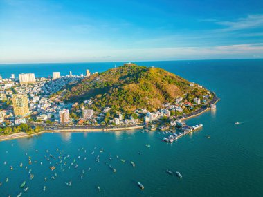 Vung Tau city aerial view with beautiful sunset and so many boats. Panoramic coastal Vung Tau view from above, with waves, coastline, streets, coconut trees and Tao Phung mountain in Vietnam.