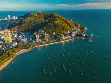 Vung Tau city aerial view with beautiful sunset and so many boats. Panoramic coastal Vung Tau view from above, with waves, coastline, streets, coconut trees and Tao Phung mountain in Vietnam.