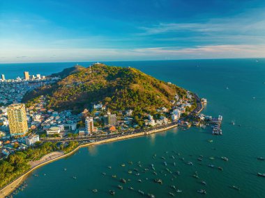Vung Tau city aerial view with beautiful sunset and so many boats. Panoramic coastal Vung Tau view from above, with waves, coastline, streets, coconut trees and Tao Phung mountain in Vietnam.