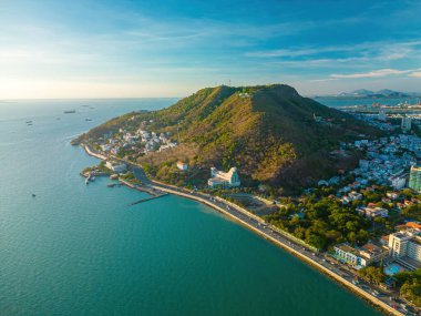 Vung Tau city aerial view with beautiful sunset and so many boats. Panoramic coastal Vung Tau view from above, with waves, coastline, streets, coconut trees and Tao Phung mountain in Vietnam.