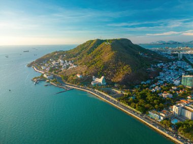 Vung Tau city aerial view with beautiful sunset and so many boats. Panoramic coastal Vung Tau view from above, with waves, coastline, streets, coconut trees and Tao Phung mountain in Vietnam.
