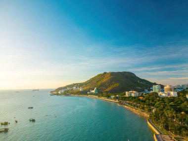 Vung Tau city aerial view with beautiful sunset and so many boats. Panoramic coastal Vung Tau view from above, with waves, coastline, streets, coconut trees and Tao Phung mountain in Vietnam.