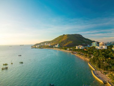 Vung Tau city aerial view with beautiful sunset and so many boats. Panoramic coastal Vung Tau view from above, with waves, coastline, streets, coconut trees and Tao Phung mountain in Vietnam.