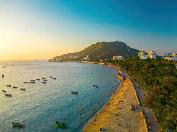 Vung Tau city aerial view with beautiful sunset and so many boats. Panoramic coastal Vung Tau view from above, with waves, coastline, streets, coconut trees and Tao Phung mountain in Vietnam.
