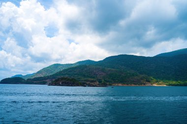 Panoramik sahil kıyısı Con Dao adası yukarıdan, dalgalar, kıyı şeridi, açık gökyüzü ve yol, mavi deniz ve dağ.