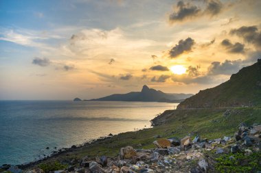 Panoramik Con Dao adası manzaralı, dalgalar, kıyı şeridi, açık gökyüzü ve yol, mavi deniz ve dağ. Bai Nhat Sahili 'nin havadan görünüşü ve sinematik gün batımı..