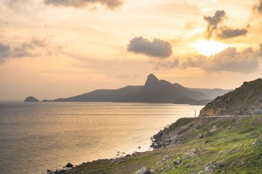 Panoramik Con Dao adası manzaralı, dalgalar, kıyı şeridi, açık gökyüzü ve yol, mavi deniz ve dağ. Bai Nhat Sahili 'nin havadan görünüşü ve sinematik gün batımı..