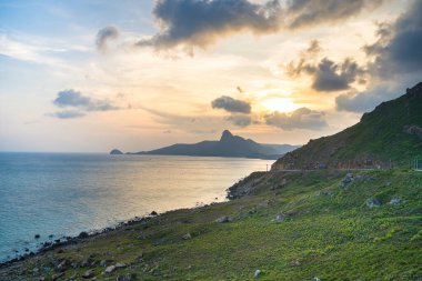 Panoramik Con Dao adası manzaralı, dalgalar, kıyı şeridi, açık gökyüzü ve yol, mavi deniz ve dağ. Bai Nhat Sahili 'nin havadan görünüşü ve sinematik gün batımı..