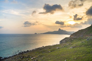 Panoramik Con Dao adası manzaralı, dalgalar, kıyı şeridi, açık gökyüzü ve yol, mavi deniz ve dağ. Bai Nhat Sahili 'nin havadan görünüşü ve sinematik gün batımı..
