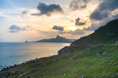 Panoramik Con Dao adası manzaralı, dalgalar, kıyı şeridi, açık gökyüzü ve yol, mavi deniz ve dağ. Bai Nhat Sahili 'nin havadan görünüşü ve sinematik gün batımı..