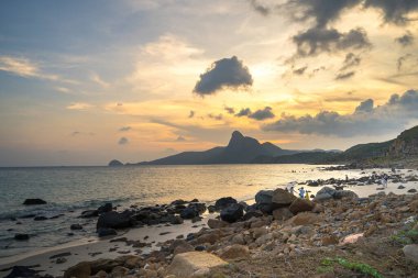 Panoramik Con Dao adası manzaralı, dalgalar, kıyı şeridi, açık gökyüzü ve yol, mavi deniz ve dağ. Bai Nhat Sahili 'nin havadan görünüşü ve sinematik gün batımı..