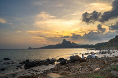 Panoramik Con Dao adası manzaralı, dalgalar, kıyı şeridi, açık gökyüzü ve yol, mavi deniz ve dağ. Bai Nhat Sahili 'nin havadan görünüşü ve sinematik gün batımı..