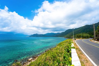 Panoramik Con Dao adası manzaralı, dalgalar, kıyı şeridi, açık gökyüzü ve yol, mavi deniz ve dağ. Vietnam 'da bir adada gün batımında gidilecek mükemmel bir yol..