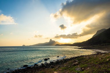 Panoramik Con Dao adası manzaralı, dalgalar, kıyı şeridi, açık gökyüzü ve yol, mavi deniz ve dağ. Bai Nhat Sahili 'nin havadan görünüşü ve sinematik gün batımı..