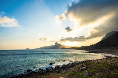 Panoramik Con Dao adası manzaralı, dalgalar, kıyı şeridi, açık gökyüzü ve yol, mavi deniz ve dağ. Bai Nhat Sahili 'nin havadan görünüşü ve sinematik gün batımı..