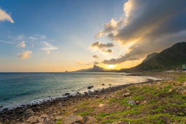 Panoramik Con Dao adası manzaralı, dalgalar, kıyı şeridi, açık gökyüzü ve yol, mavi deniz ve dağ. Bai Nhat Sahili 'nin havadan görünüşü ve sinematik gün batımı..