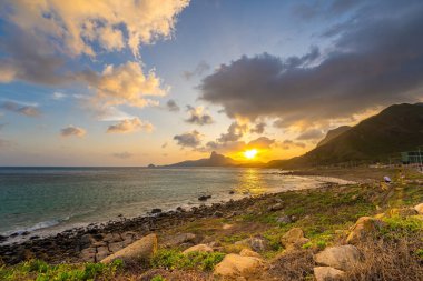 Panoramik Con Dao adası manzaralı, dalgalar, kıyı şeridi, açık gökyüzü ve yol, mavi deniz ve dağ. Bai Nhat Sahili 'nin havadan görünüşü ve sinematik gün batımı..