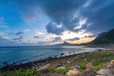 Panoramik Con Dao adası manzaralı, dalgalar, kıyı şeridi, açık gökyüzü ve yol, mavi deniz ve dağ. Bai Nhat Sahili 'nin havadan görünüşü ve sinematik gün batımı..