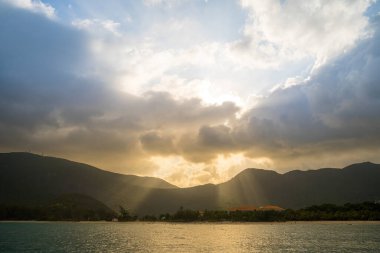 Güneş batarken sakin deniz Con Dao Adası üzerindeki bulutların arasından. Gün batımında gökyüzü ve bulutların arasında güneş olan sakin bir deniz. Meditasyon okyanusu ve gökyüzü arka planı. Huzurlu deniz manzarası.
