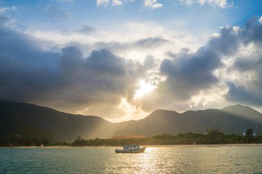 Güneş batarken sakin deniz Con Dao Adası üzerindeki bulutların arasından. Gün batımında gökyüzü ve bulutların arasında güneş olan sakin bir deniz. Meditasyon okyanusu ve gökyüzü arka planı. Huzurlu deniz manzarası.
