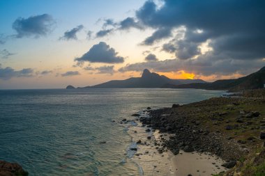 Panoramik Con Dao adası manzaralı, dalgalar, kıyı şeridi, açık gökyüzü ve yol, mavi deniz ve dağ. Bai Nhat Sahili 'nin havadan görünüşü ve sinematik gün batımı..