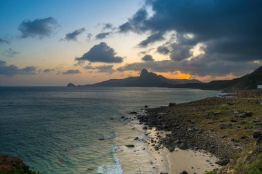 Panoramik Con Dao adası manzaralı, dalgalar, kıyı şeridi, açık gökyüzü ve yol, mavi deniz ve dağ. Bai Nhat Sahili 'nin havadan görünüşü ve sinematik gün batımı..