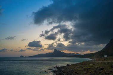 Panoramik Con Dao adası manzaralı, dalgalar, kıyı şeridi, açık gökyüzü ve yol, mavi deniz ve dağ. Bai Nhat Sahili 'nin havadan görünüşü ve sinematik gün batımı..