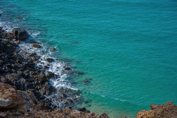 空中俯瞰海浪和美丽的落基海岸 美丽清澈的水下表面 海底岩石在透明的蓝水下 清澈的蓝绿色海面上有太阳光反射的波纹 — 图库照片