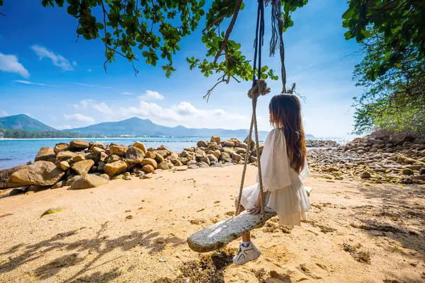 背景にヤシの木とインドのアーモンドの木とターコイズブルーの海とビーチでスイングに座って旅行の女性のバックビュー 夏休み 熱帯の休日 旅行とライフスタイルのコンセプト — ストック写真