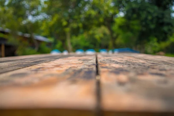 空の木のテーブルにフォーカスを当て 緑の森の景色はボケのイメージで背景をぼかす 写真のモンタージュや商品のために 空茶色の木製のテーブルとキャンプのぼかしの背景 — ストック写真