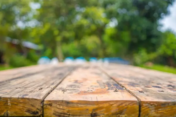 空の木のテーブルにフォーカスを当て 緑の森の景色はボケのイメージで背景をぼかす 写真のモンタージュや商品のために 空茶色の木製のテーブルとキャンプのぼかしの背景 — ストック写真